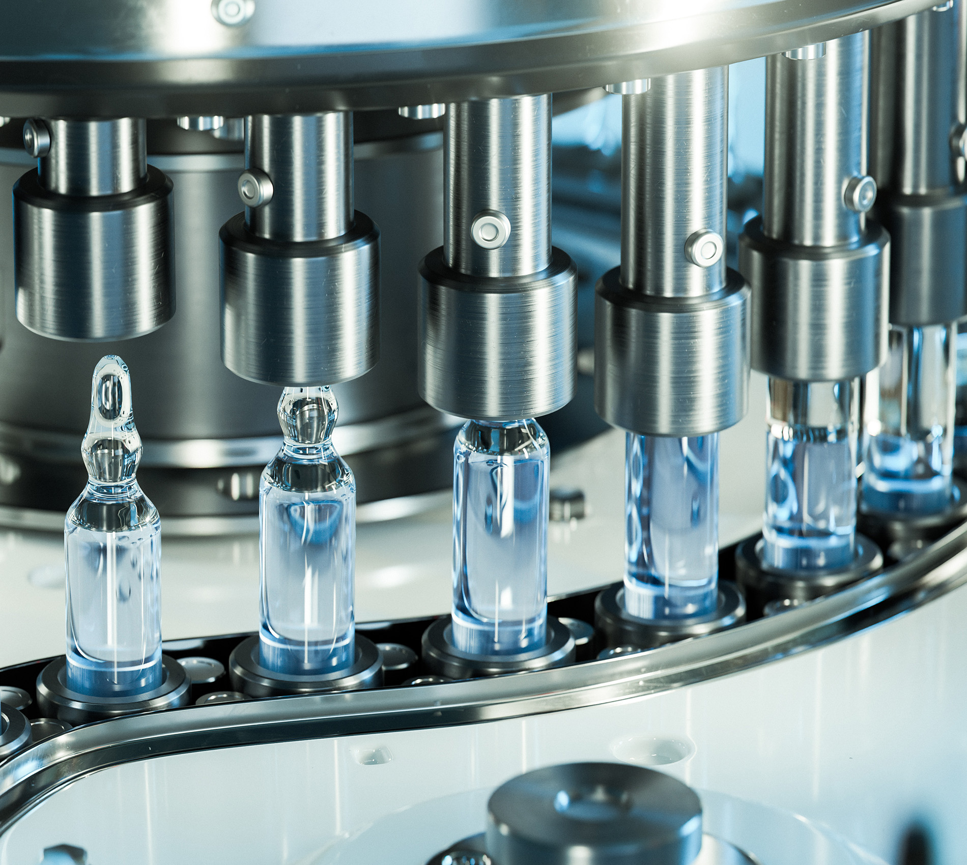 Nahaufnahme einer industriellen Abfüllanlage mit mehreren Glasfläschchen auf einem Förderband unter metallischen Maschinenköpfen.